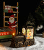 Decorative train lamp with Christmas scene inside, surrounded by festive items on a dark background.