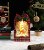 Decorative Christmas lantern with plaid design in front of a Christmas tree and festive decorations.
