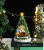 Decorative Christmas tree with lights and a small house on a black box labeled 'Winter Greens'.