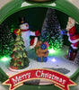 Christmas-themed miniature scene with Santa Claus, snowman, and trees inside a circular frame.