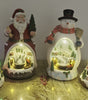 Four Christmas-themed light-up figurines on a wooden surface.