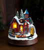 Decorative Christmas village scene with a house, trees, and people on a dark background