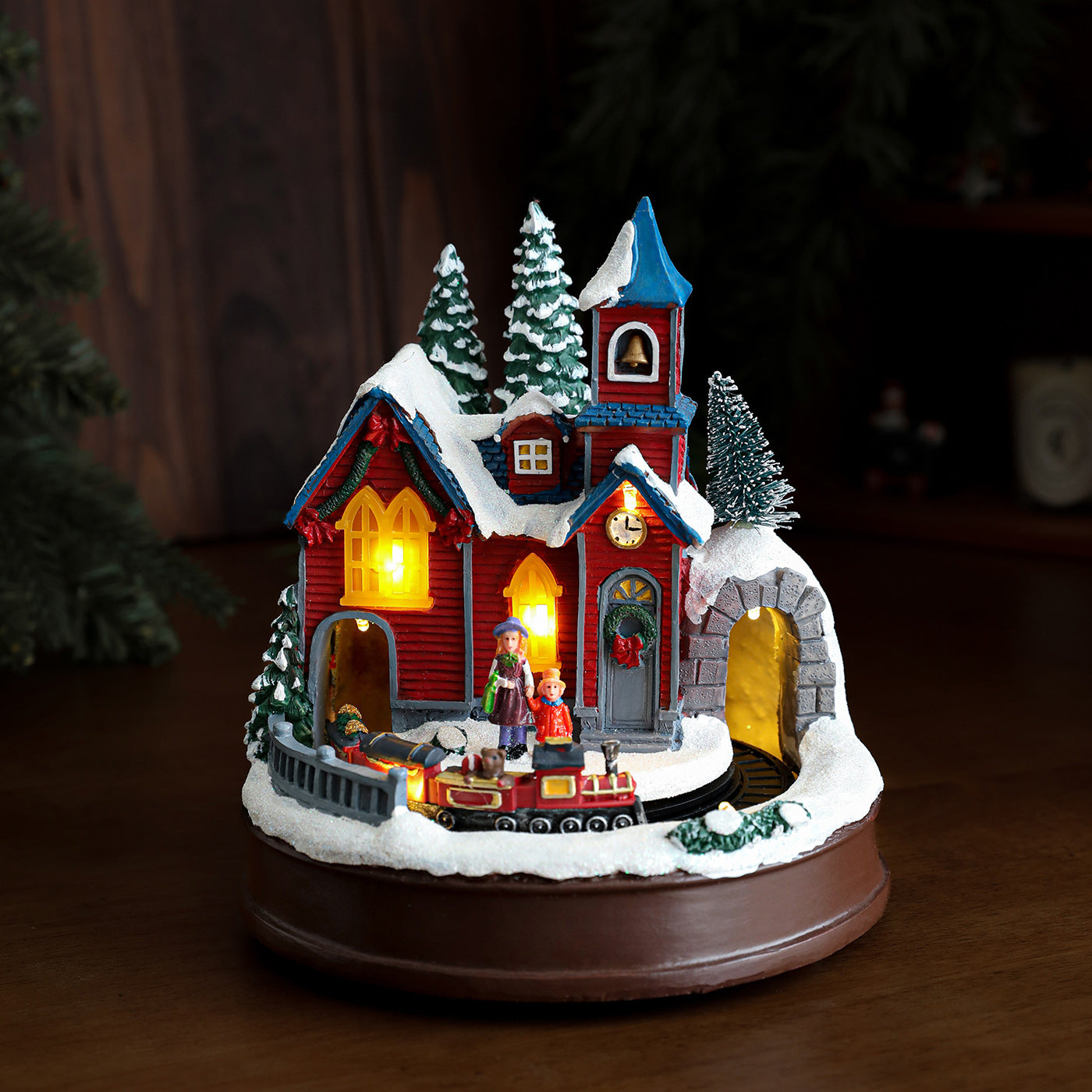 Decorative Christmas village scene with a house, trees, and people on a dark background