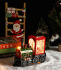 Decorative train lamp with glowing lights on a snowy surface, surrounded by Christmas decorations.