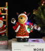 Decorative bear figurine in a Santa outfit with lights, surrounded by Christmas decorations.