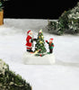 Miniature Santa Claus and child figure decorating a Christmas tree in a snowy scene.