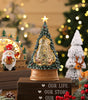 Decorative Christmas tree with lights and ornaments on a wooden base, surrounded by festive decorations.