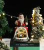 Decorative Santa Claus figure with a lit-up scene on a table with Christmas trees and lights.