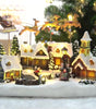 Decorative Christmas village scene with lit houses and trees on a snowy base.