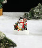 Miniature Snowman and child figure decorating a Christmas tree in a snowy scene.