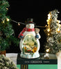 Decorative snowman with a lit scene inside, surrounded by Christmas trees and lights.
