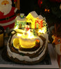 Decorative Christmas scene with a small house, snowman, and reindeer on a lit base.