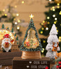 Decorative Christmas tree with lights and ornaments on a wooden base, surrounded by festive decorations.