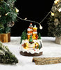 Decorative Christmas scene with a lit-up gingerbread house and trees on a snowy surface.