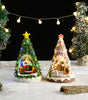 Two miniature Christmas trees with lit-up houses inside, surrounded by string lights and snow-like surface.