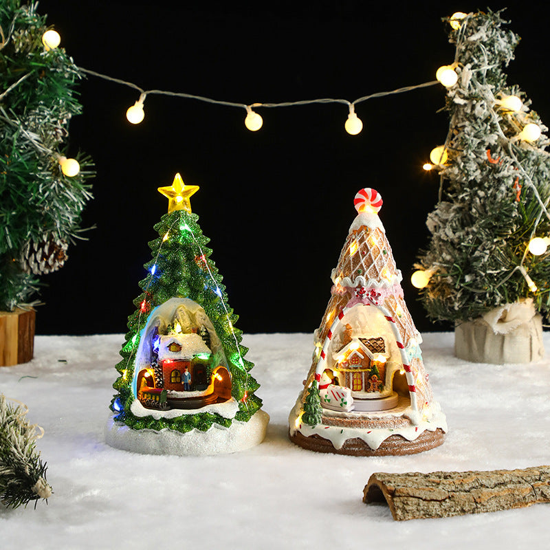 Two miniature Christmas trees with lit-up houses inside, surrounded by string lights and snow-like surface.