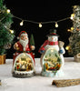 Decorative snow globe figures of Santa Claus and a snowman with Christmas trees and lights in the background.