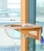 Wooden pet feeding station with glass bowl, measurements indicated, against a blurred window background.